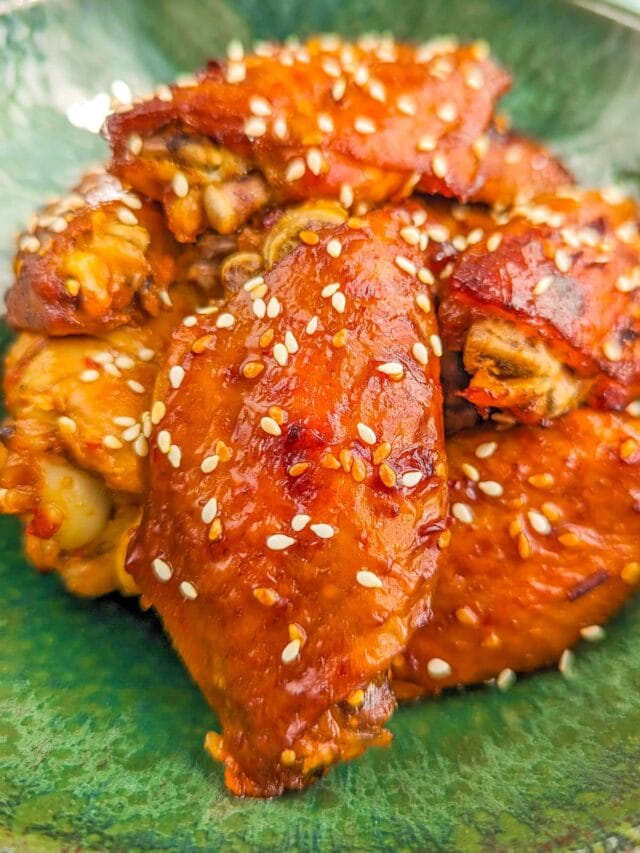 Close look of chicken wings with sesame seeds in a green plate.