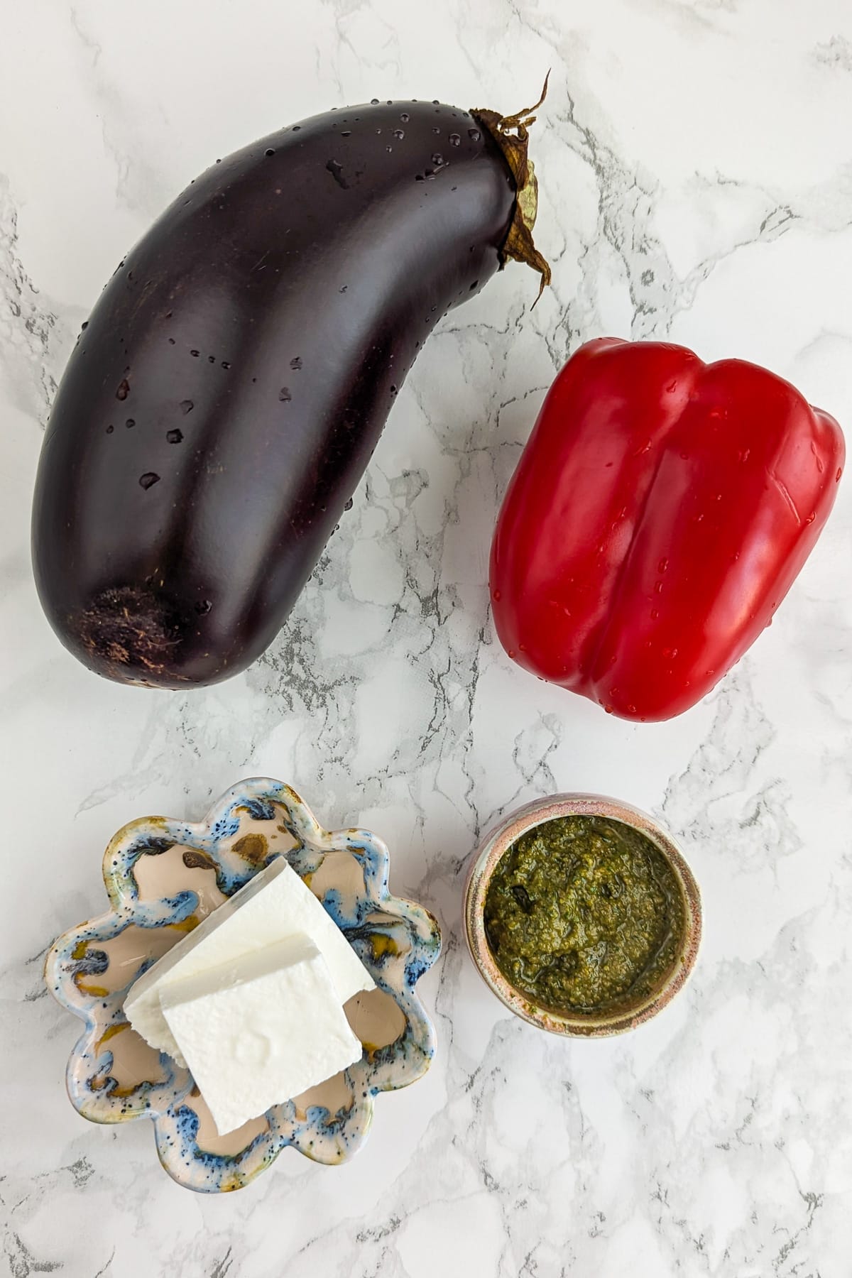 Top view of a large eggplant, bell peppers, basil pesto and two slices of feta cheese.