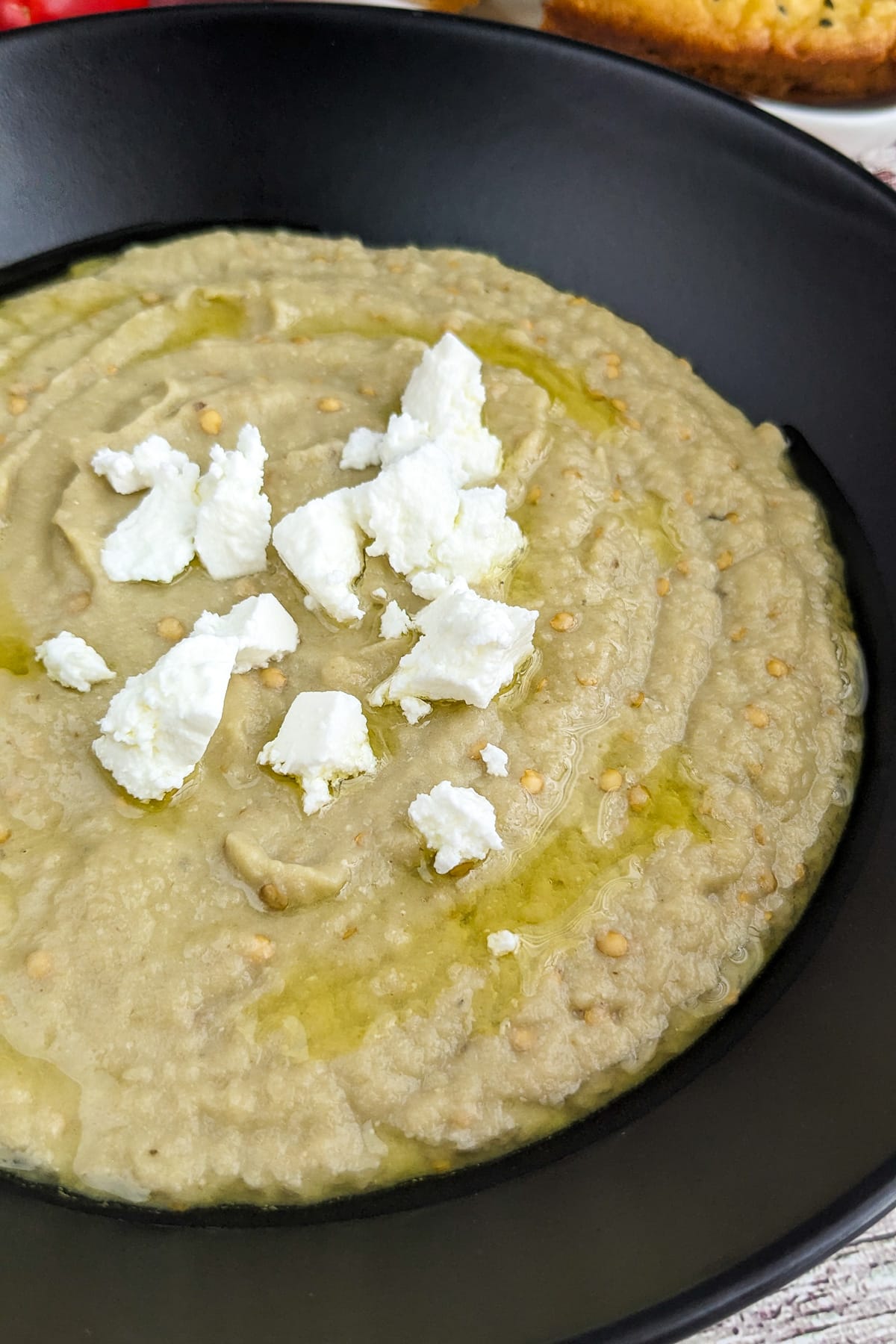 Close view of a black plate with eggplant and garlic dip with feta on a wooden table.
