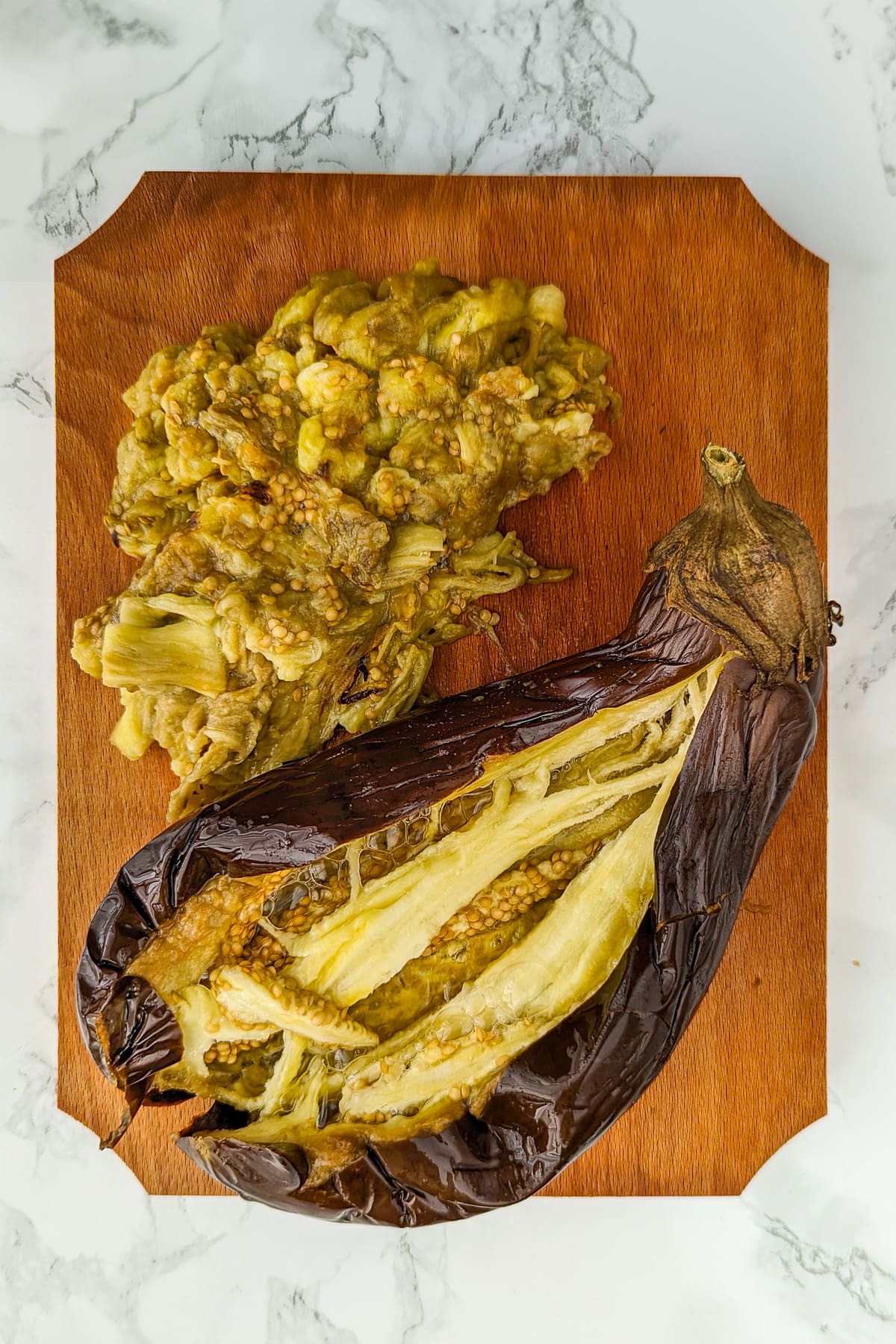 Top view of a baked eggplant on a wooden cutting board.