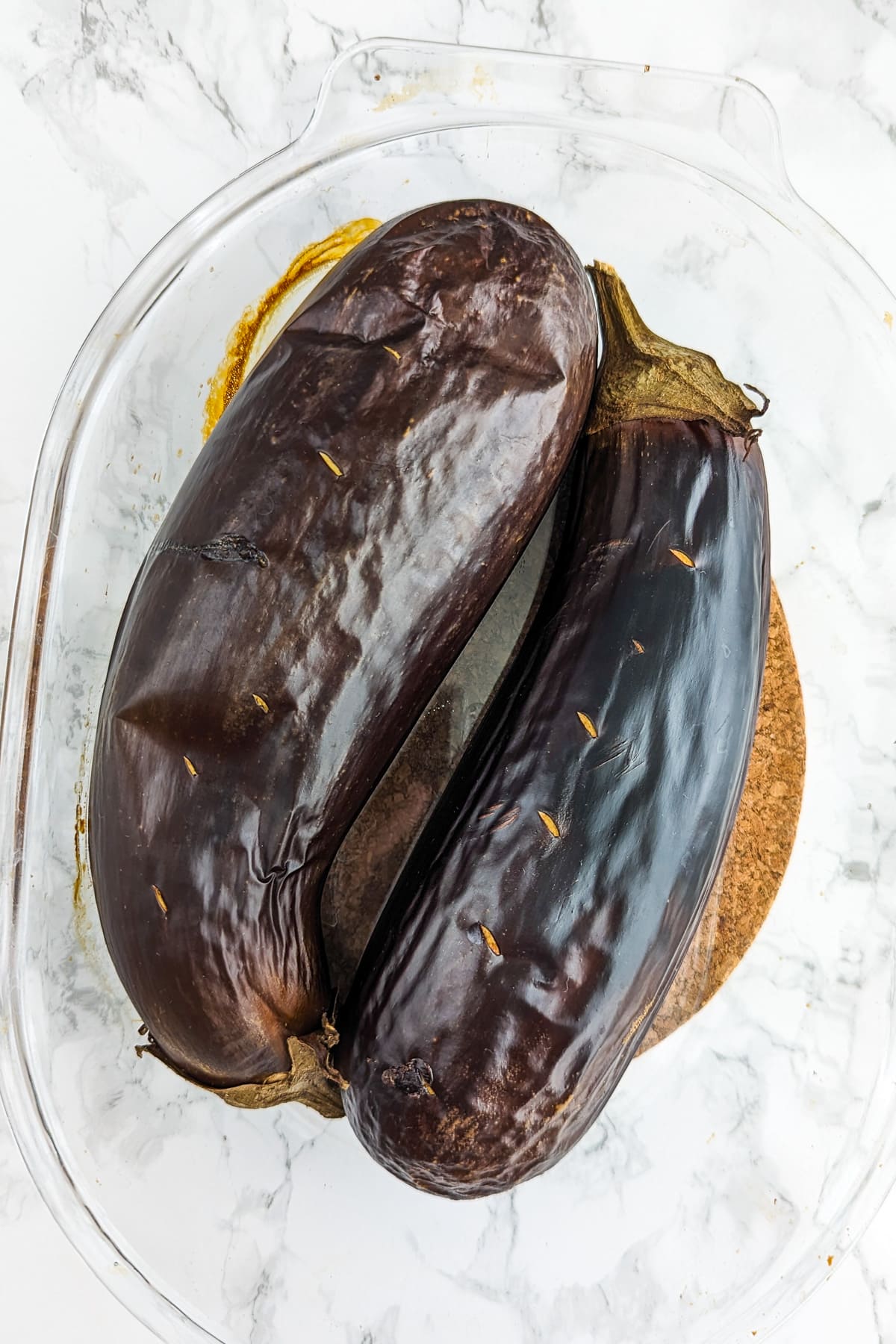 Top view of 2 baked eggplants sitting in a transparent baking dish.