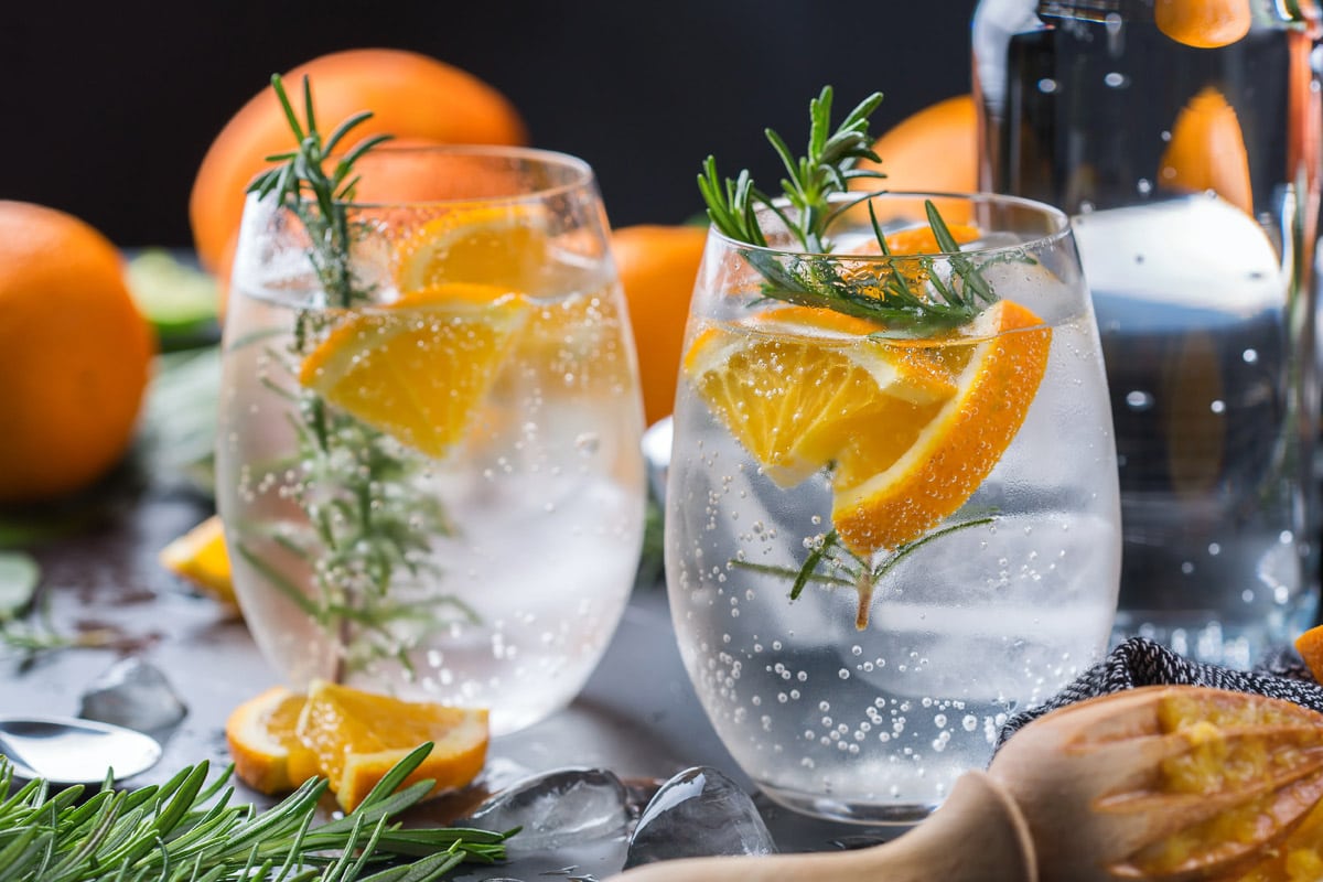 3 glass with sparkling water near some rosemary brunches and orange slices.