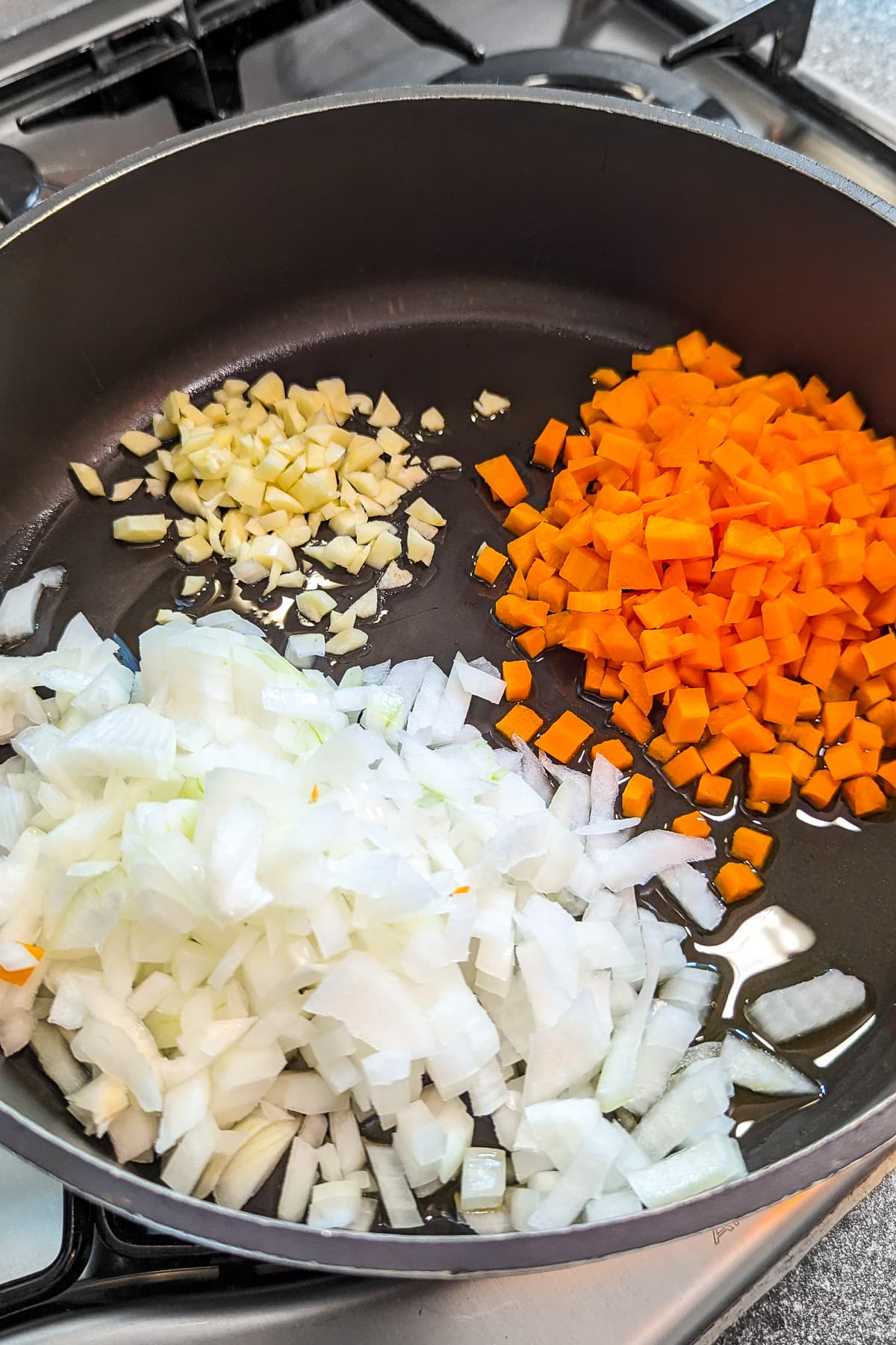 Frying chopped onions, carrots and garlic in a frying pan on the stove.