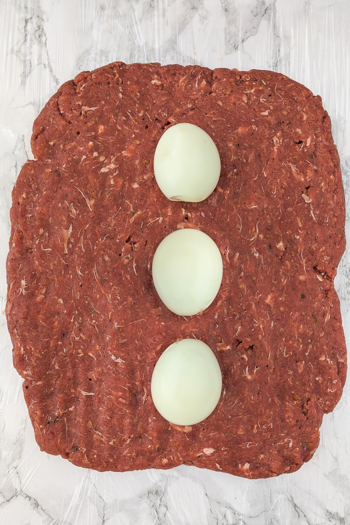 Top view of a layer of ground beef and 3 boiled eggs on it.