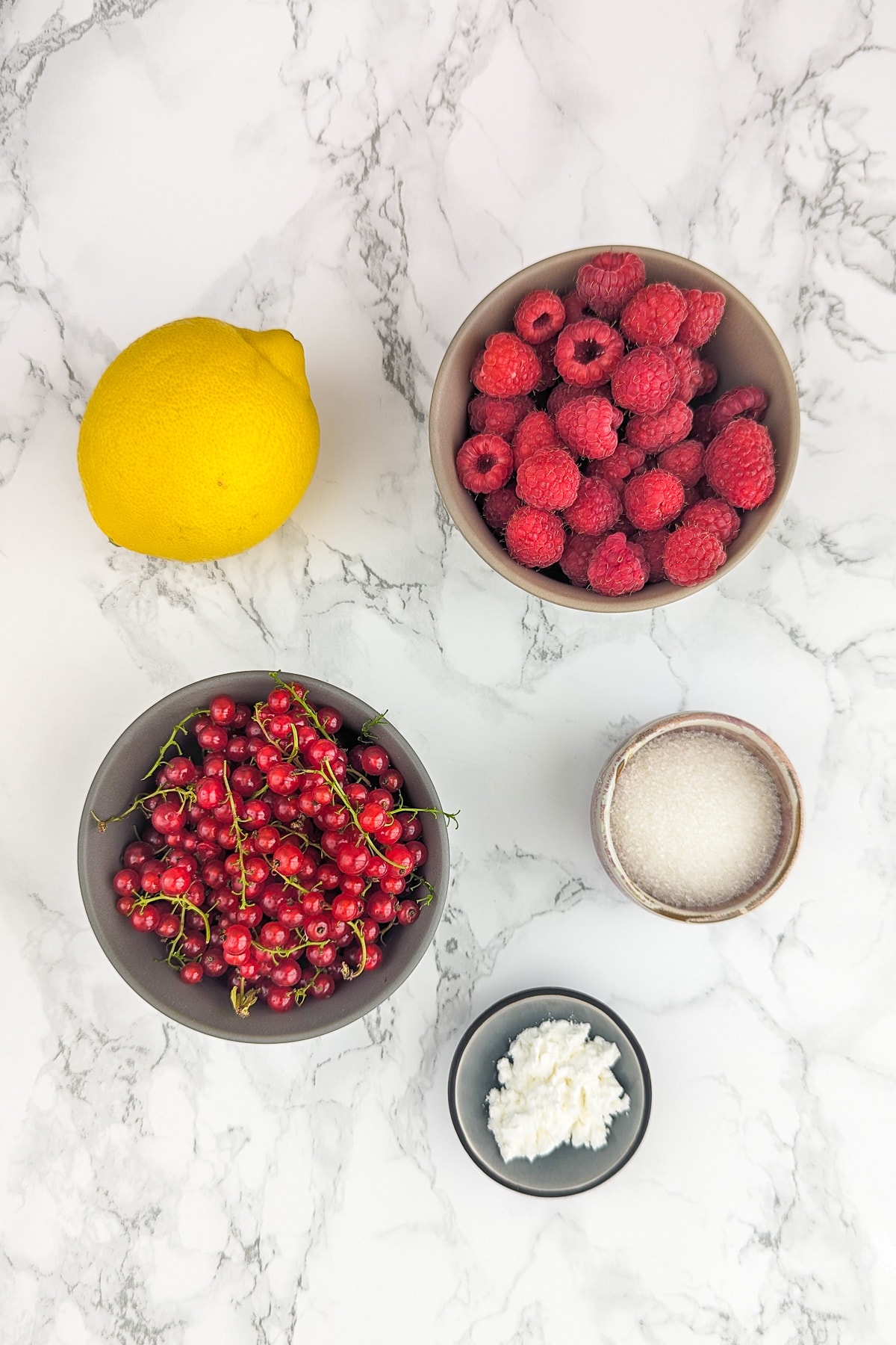 Raspberries, Red currants, sugar, lemon and starch on a white marble table.