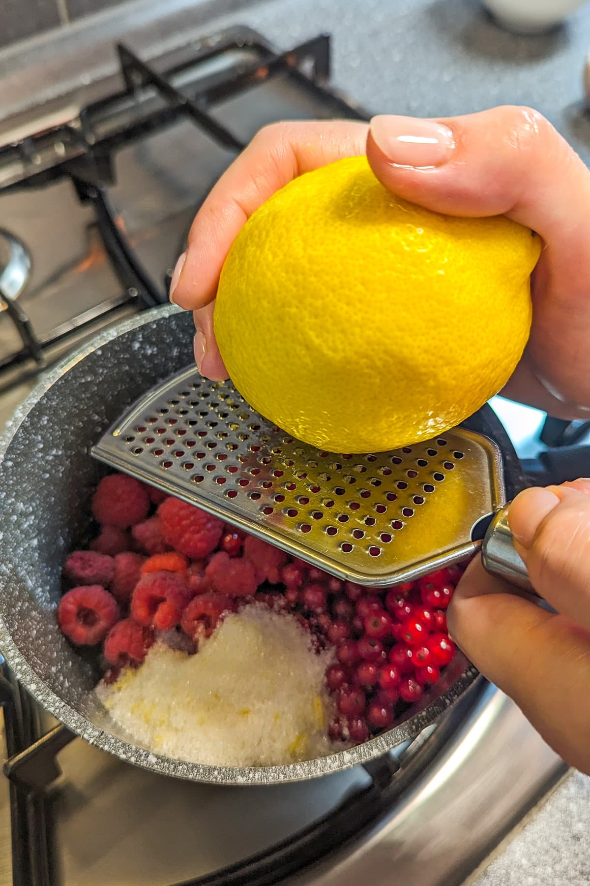Peeling lemon over a saucepan with raspberries and Red currants.