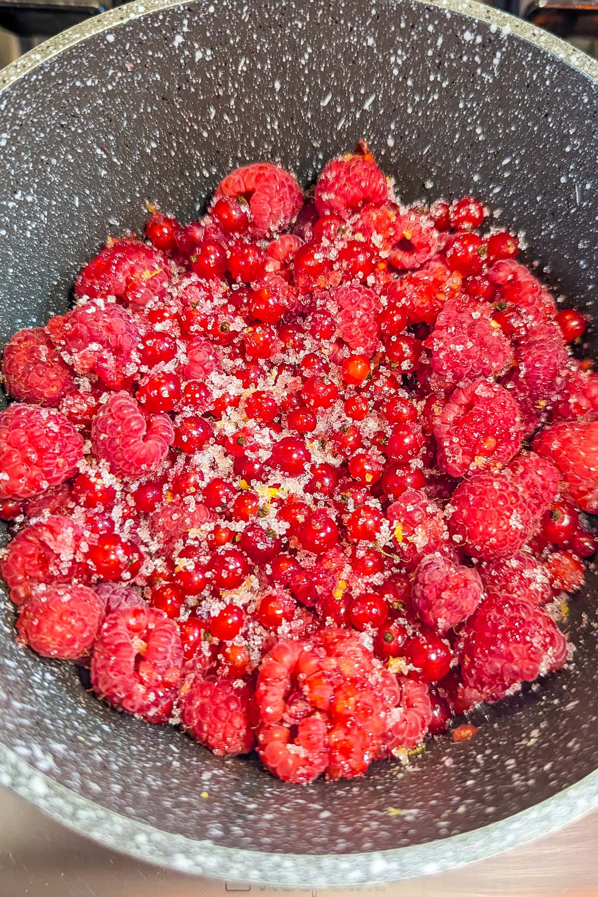 Raspberries with Red currants and lemon sugar in a saucepan.