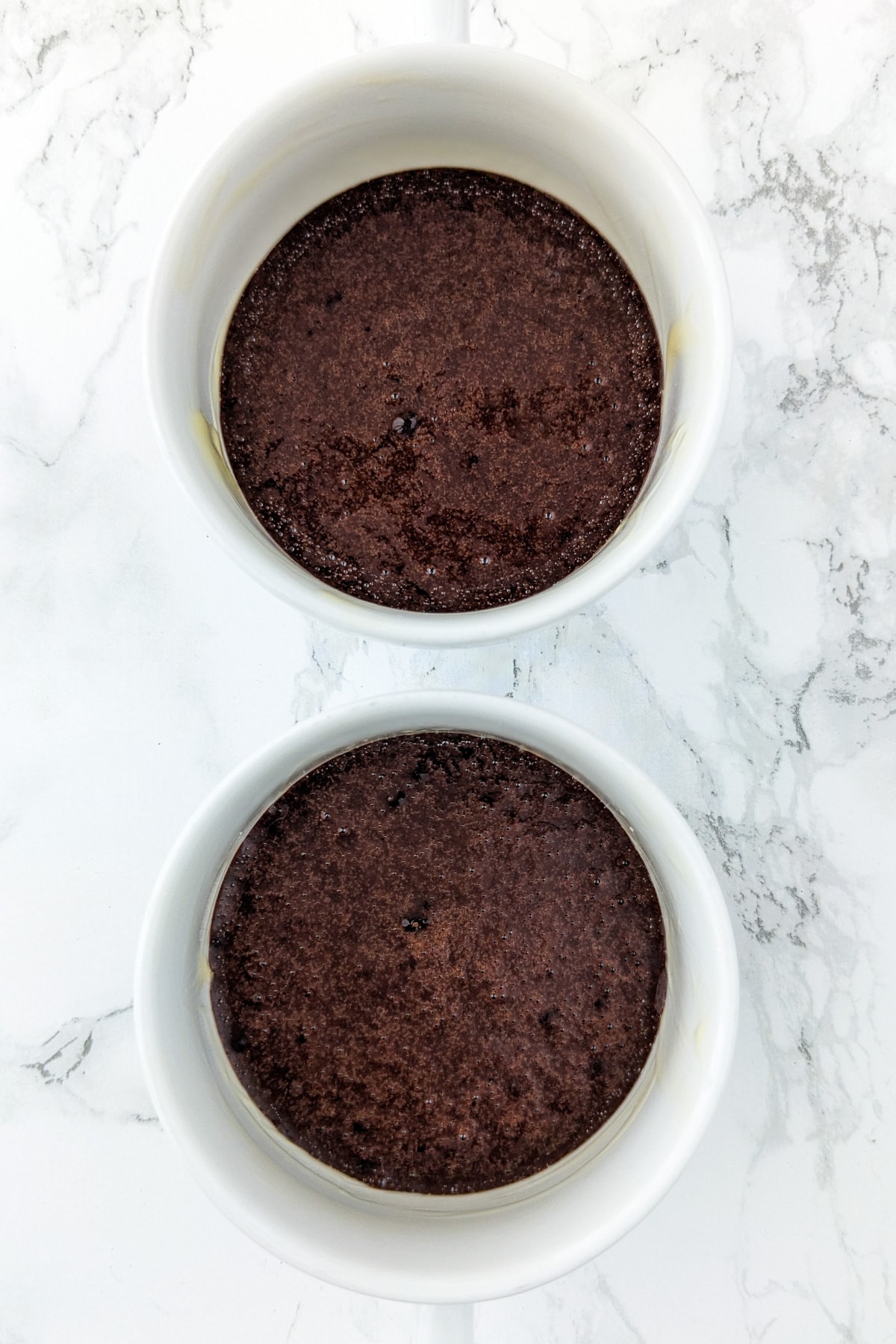 Top view of 2 mugs with chocolate cake baked in the microwave.
