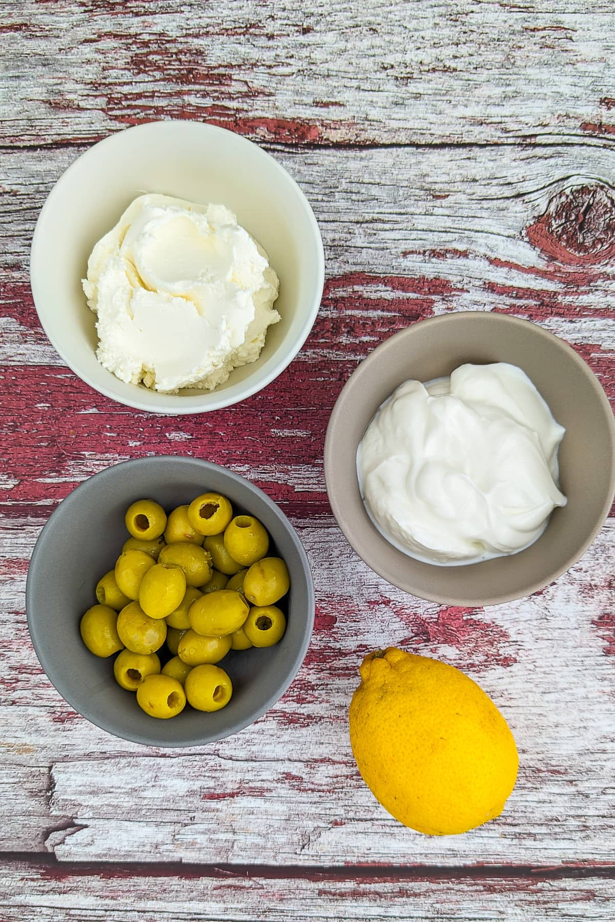 Top view of Greek yogurt, cream cheese, olives and lemon on a rustic wooden table.