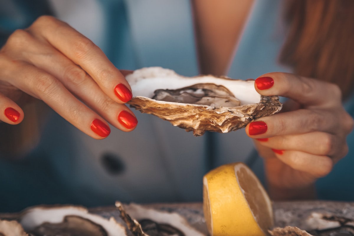 Two woman hands holding one oyster over a piece of lemon.