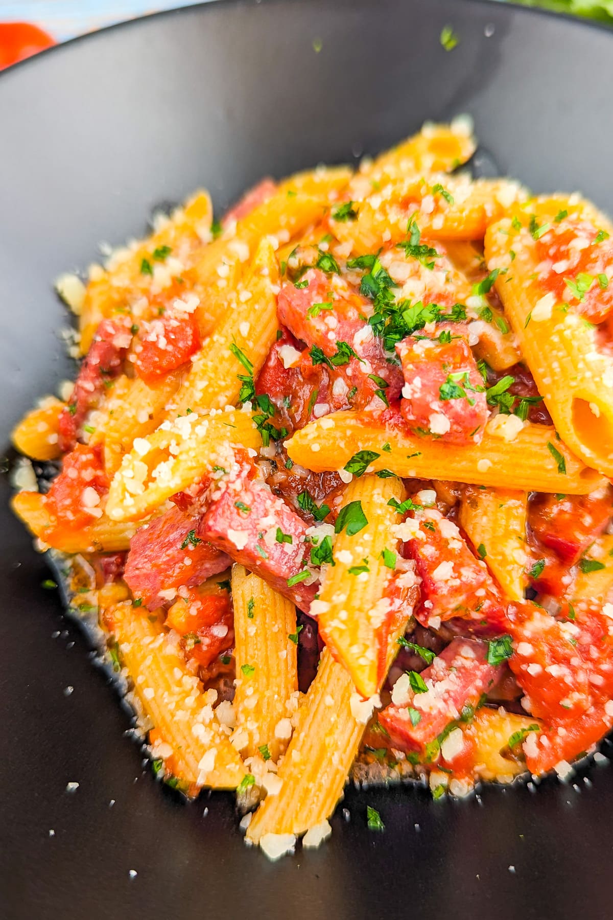 Close look of pepperoni pasta sprinkled with parsley in a black table.