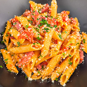 Close look of pepperoni pasta sprinkled with parsley in a black table.