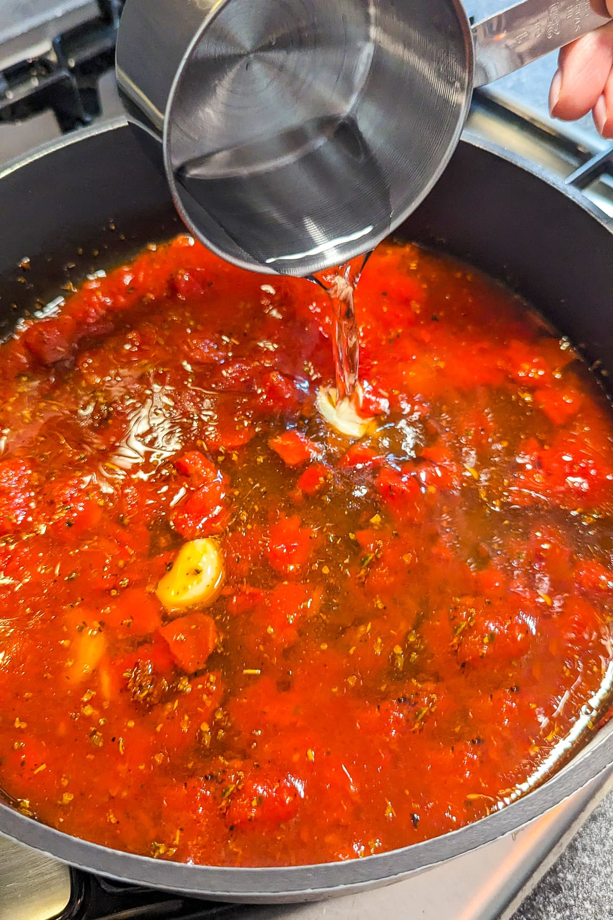 Pouring water in a pan with a tomato sauce.
