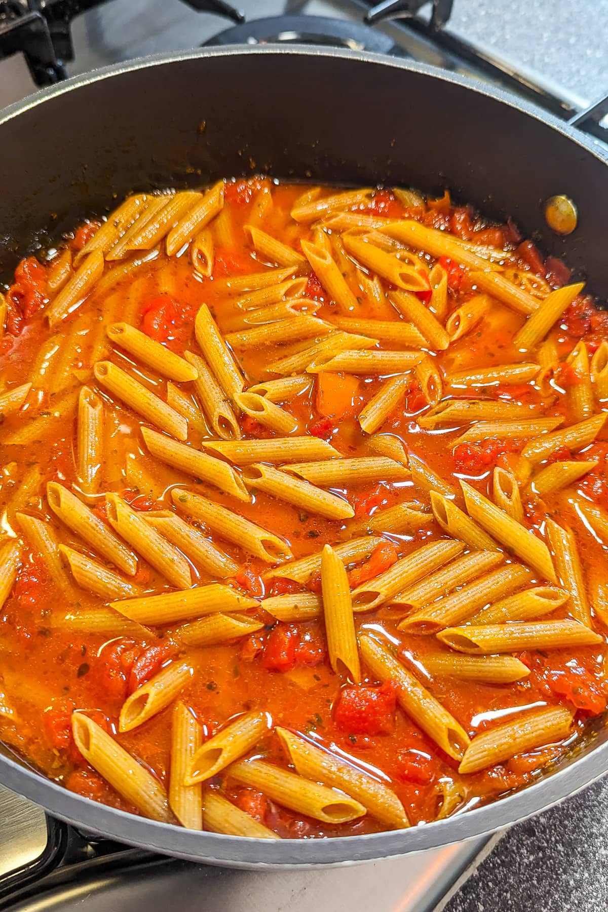 Close look of a pan with pasta and tomatoes on the stove.