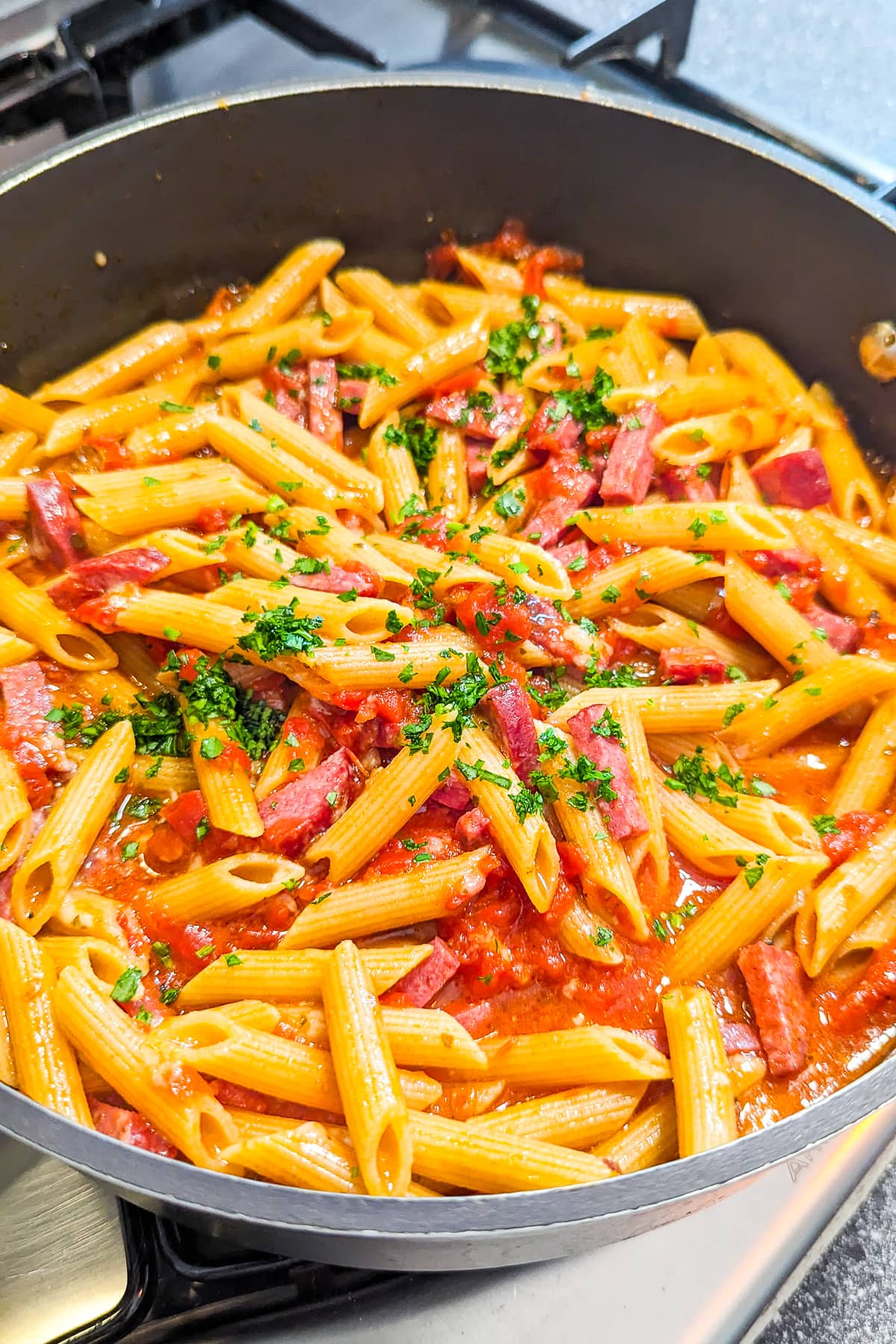 Close look of pepperoni pasta sprinkled with parsley on a pan on the stove.