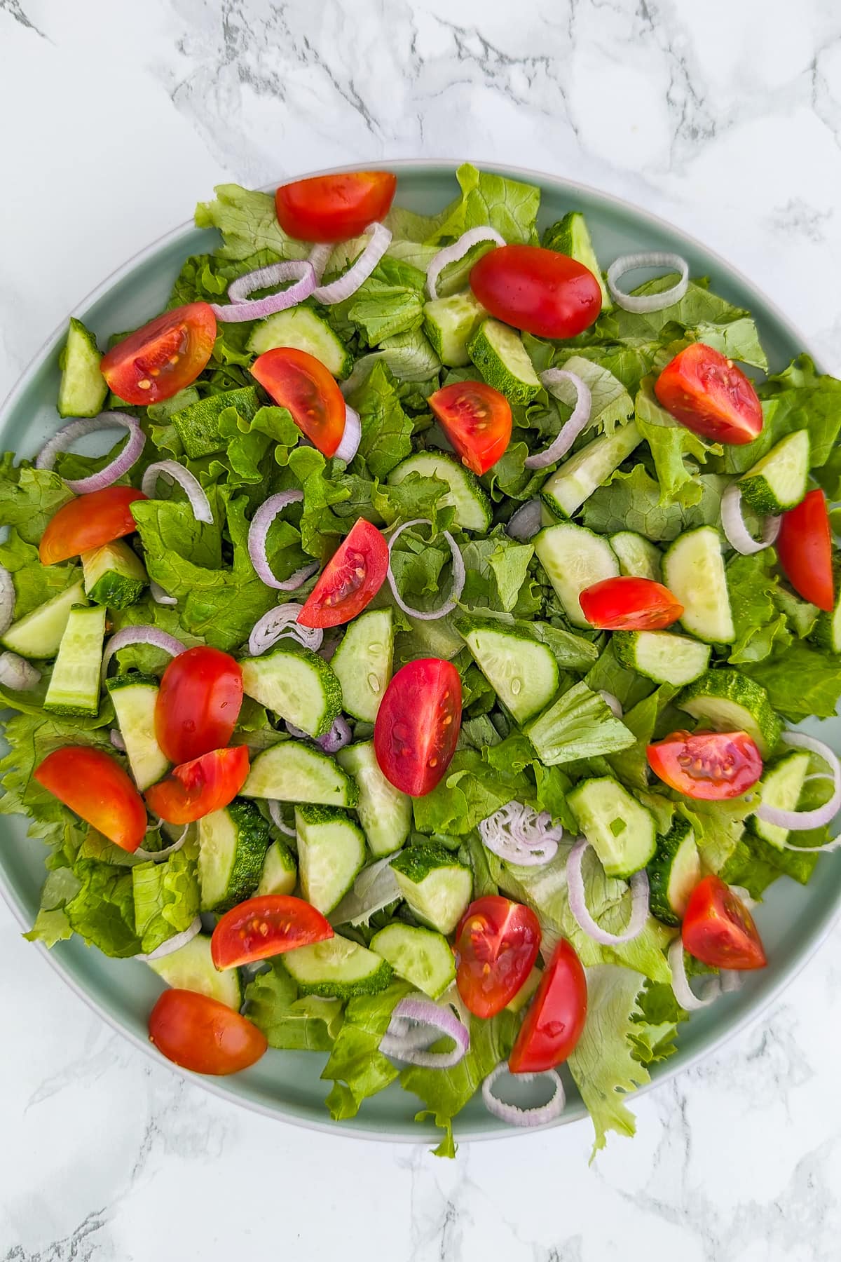 Top view of a plate with green salad with salad leaves, cucumbers, tomatoes and onions.