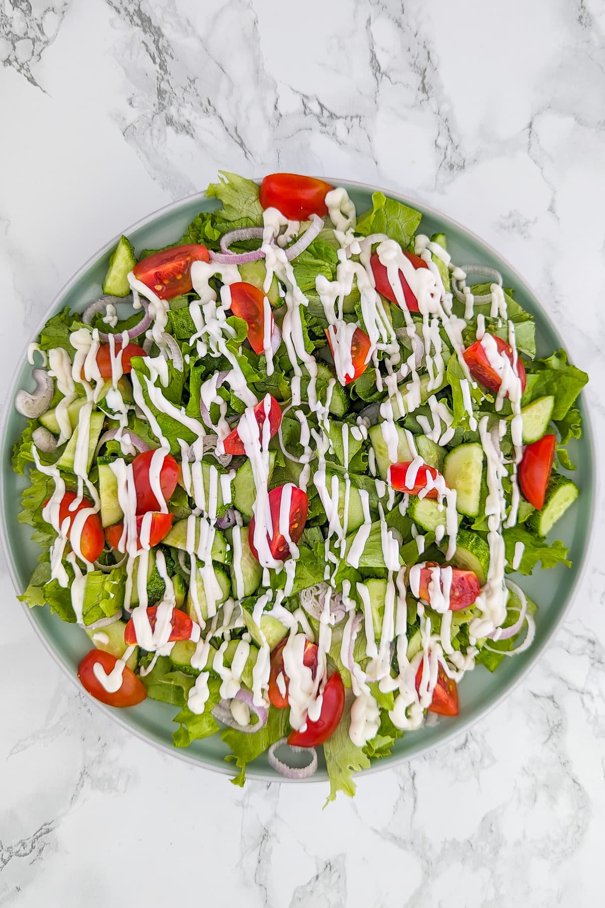 A green salad with cucumbers, salad leaves and tomatoes topped with a mix of yogurt and mayo.