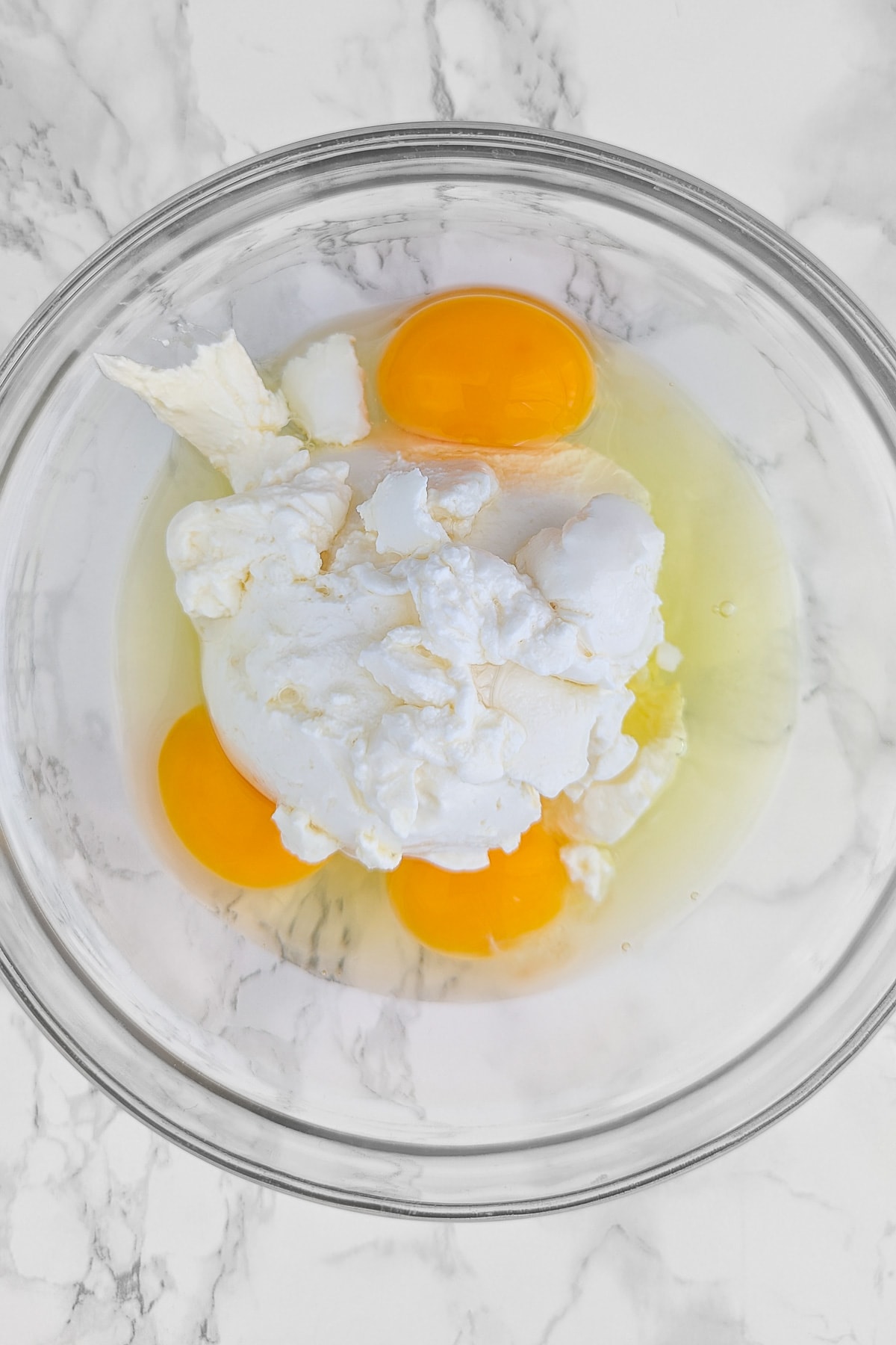 Top view of a transparent bowl with a 3 eggs and cream cheese.