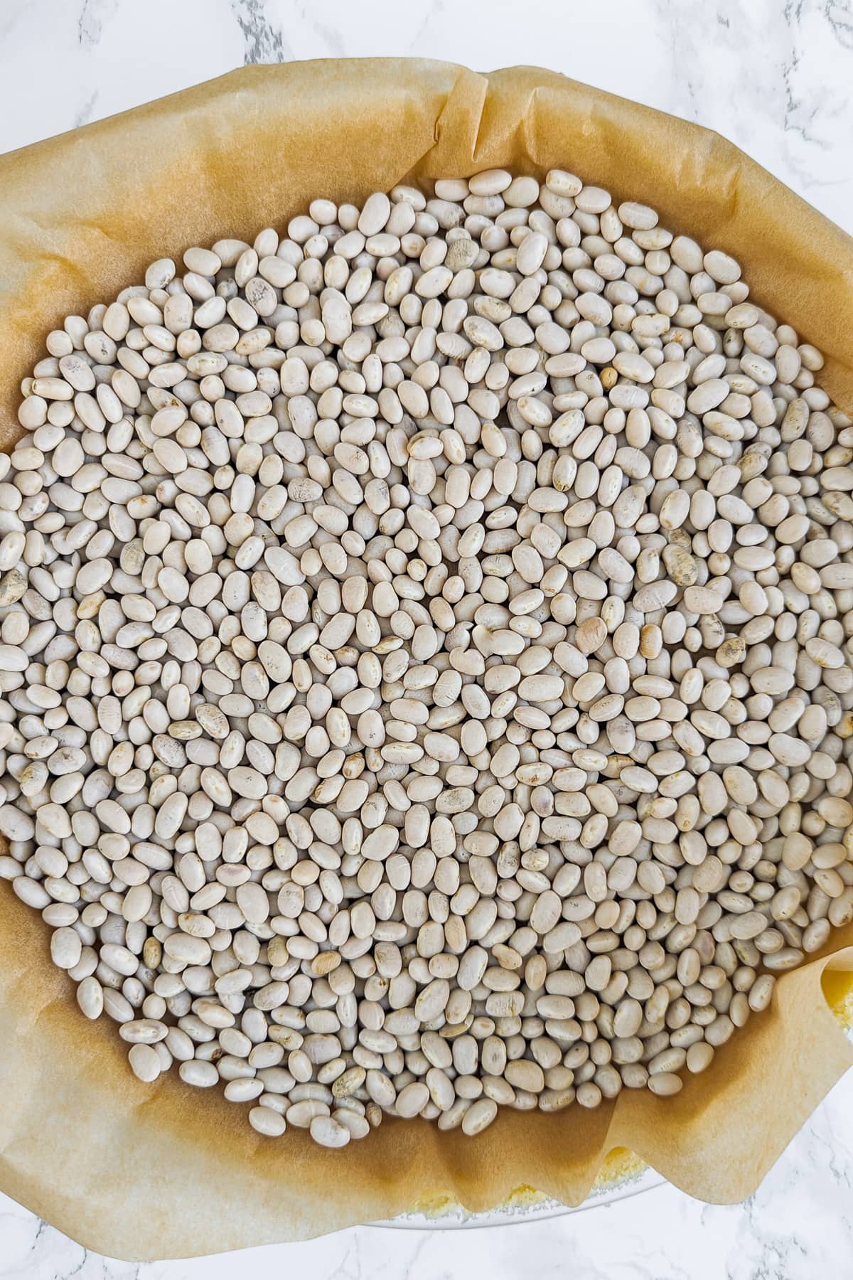 Top view of white beans on a parchment paper on a white marble table.