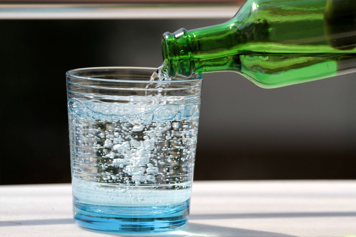 Pouring sparkling water from a green bottle into a transparent glass.