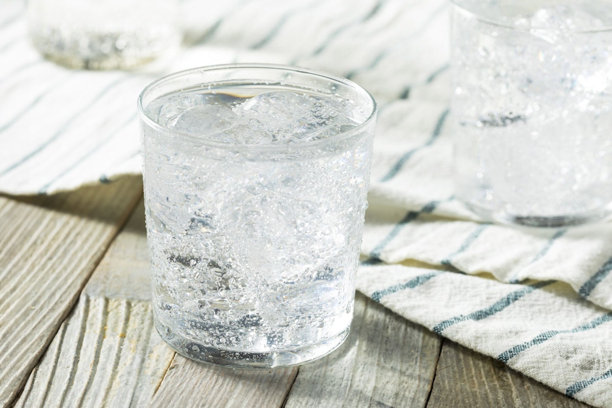 A glass with sparkling water sitting on a wooden table.