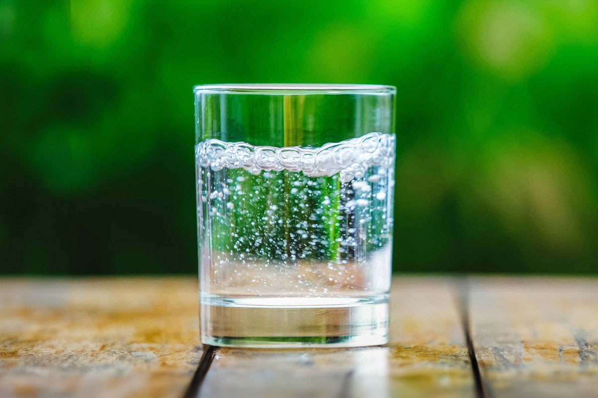 Side view of a glass with sparkling water on a green background.