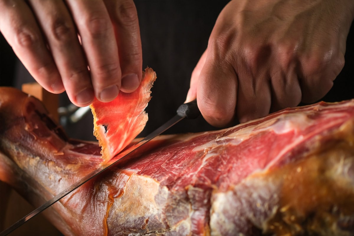 The process of slicing prosciutto with a sharp knife.