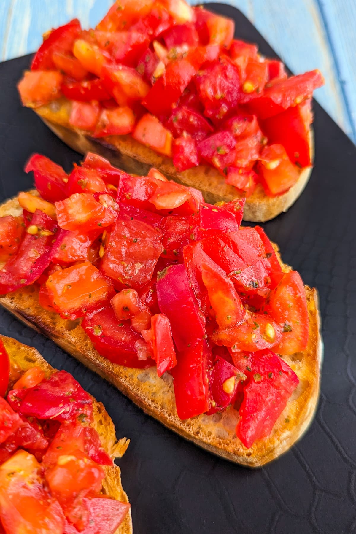 Close look of 3 slices of tomato bruschetta on a black plate.