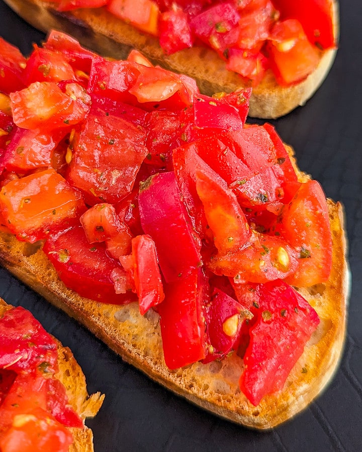 Close look of 3 slices of tomato bruschetta on a black plate.