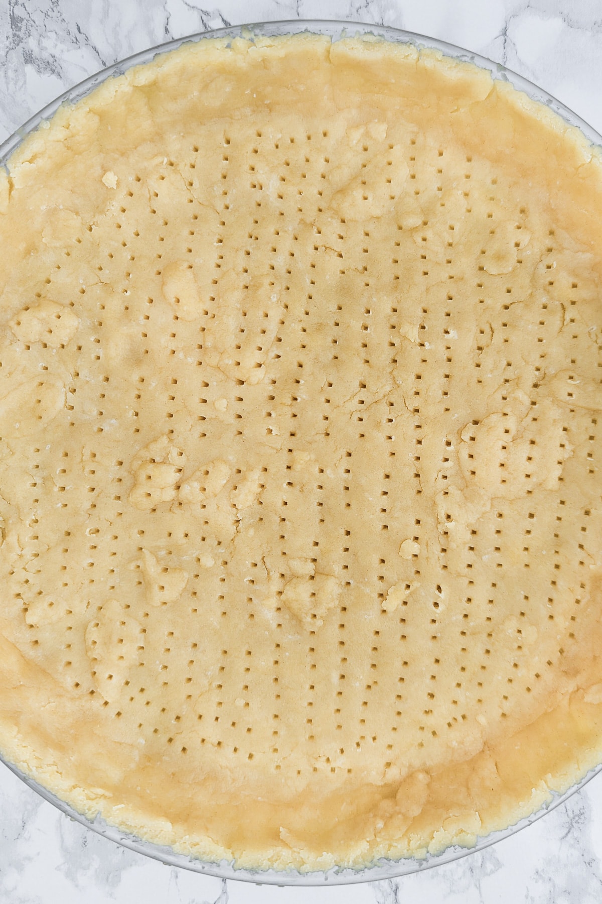 Top view of a perforated dough layered in a transparent baking dish.