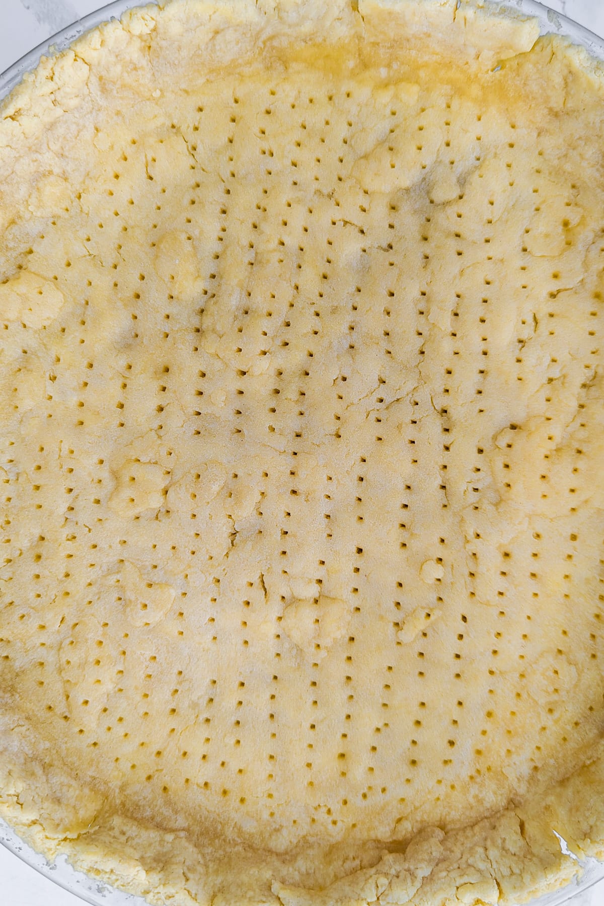 Top view of a sheet of a perforated dough layerd in a transparent baking dish.