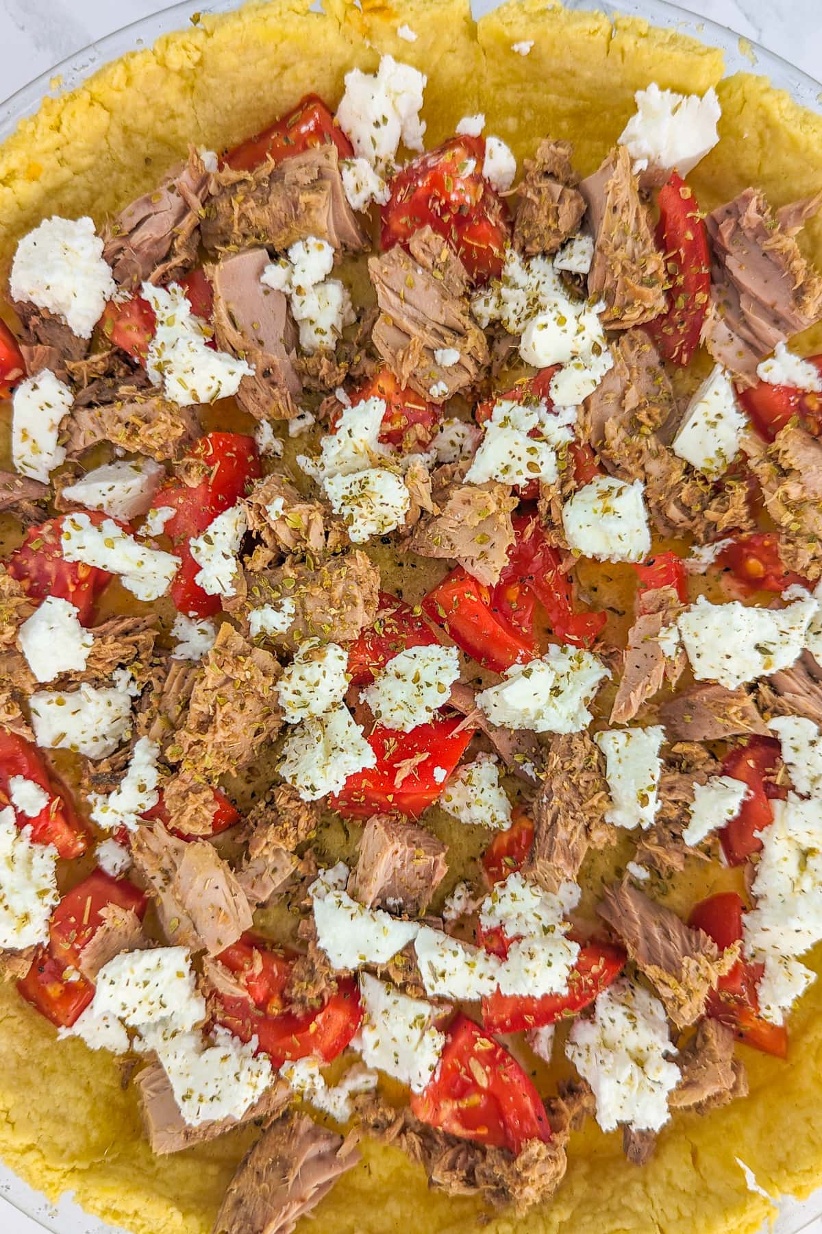 Pieces of tuna, tomatoes and feta cheese arranged on a sheet of baked dough.