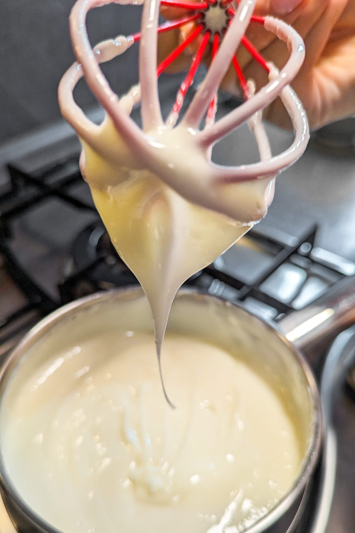 Vanila cream pouring from a red whisk over a pan with vanila cream.