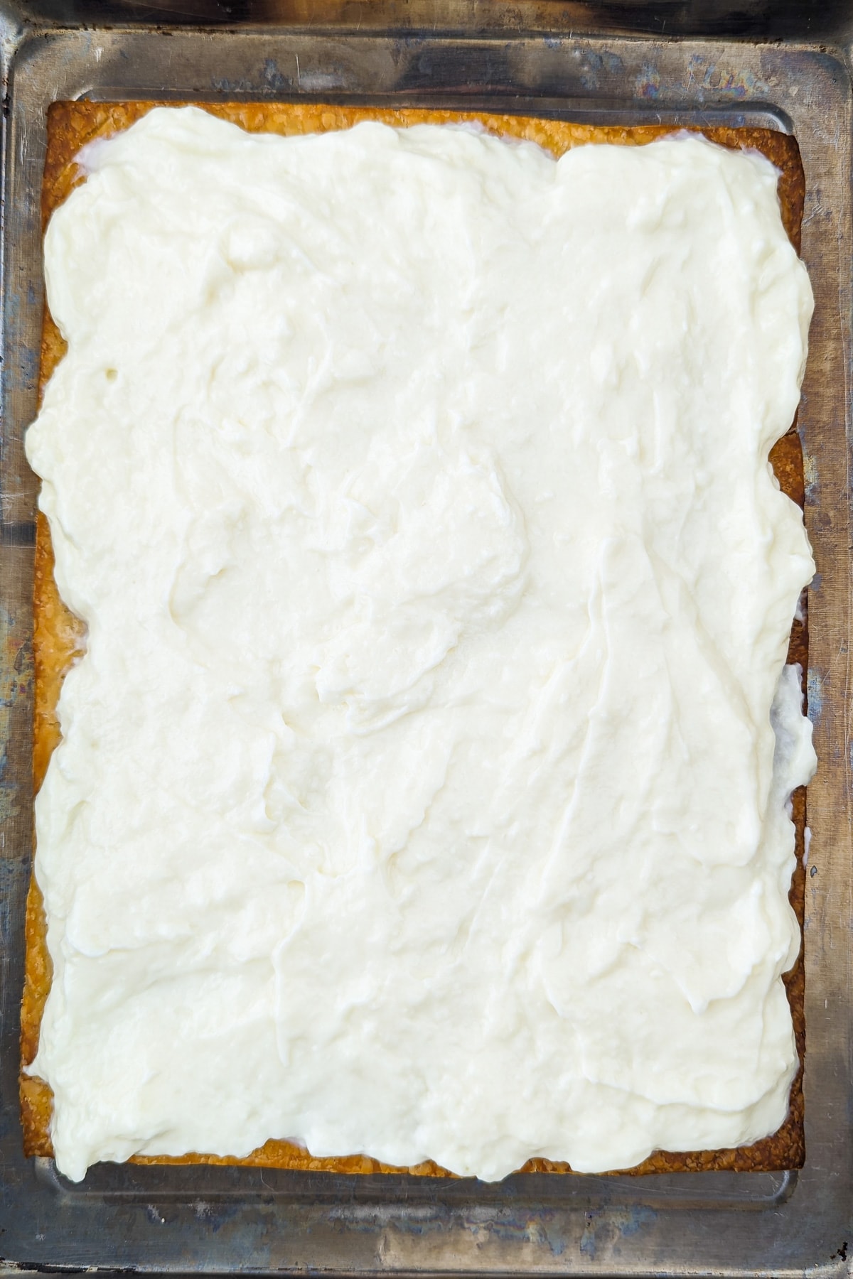 Vanilla cream topped over crunchy dough in a tray bake.