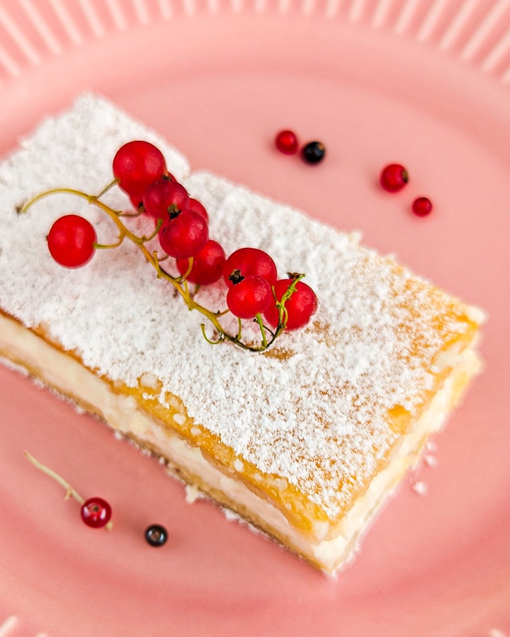 Top view of a vanila slice with cran berries on a pink plate.