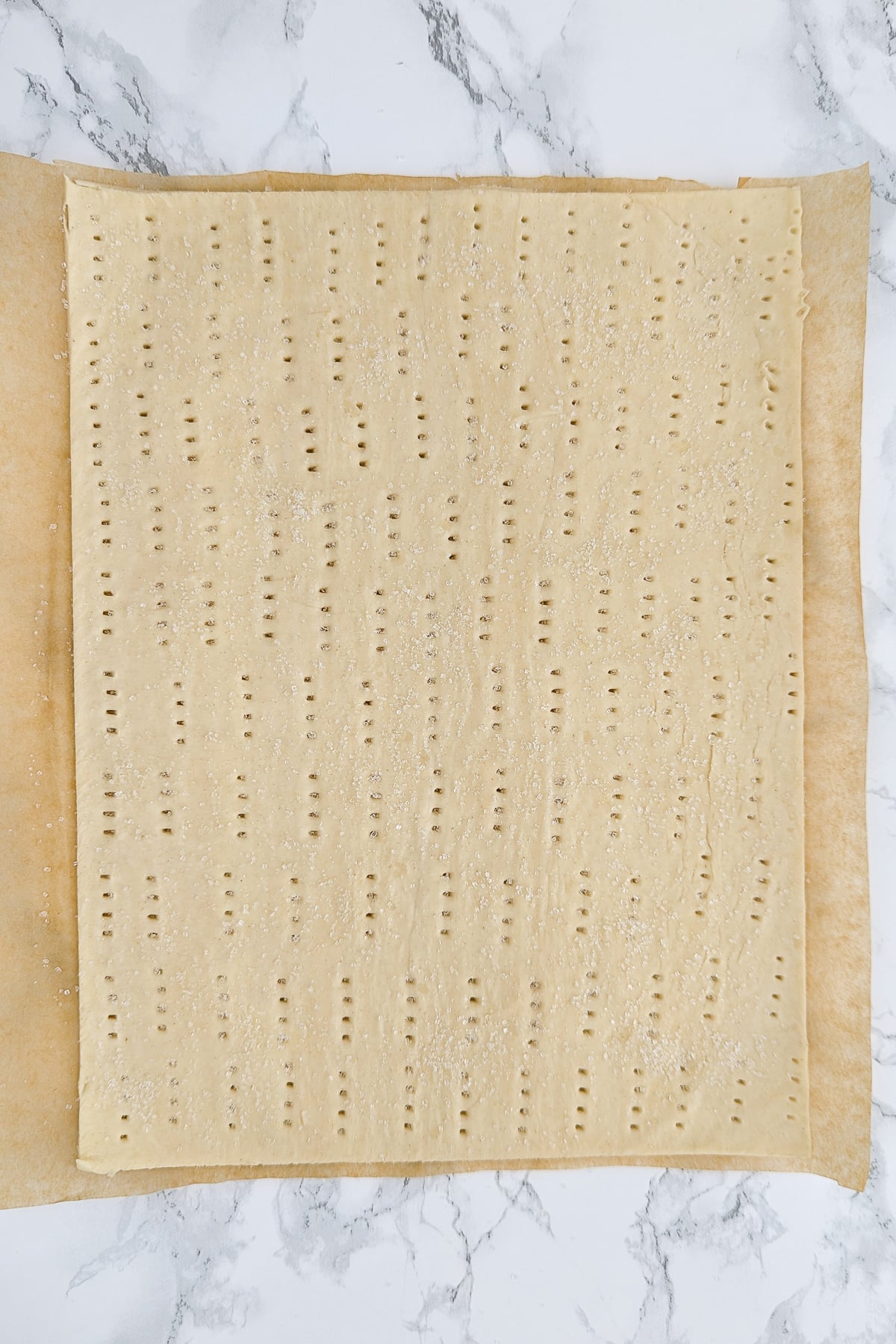 A slice of dough sprinkled with sugar on a parchment paper on a marble table.