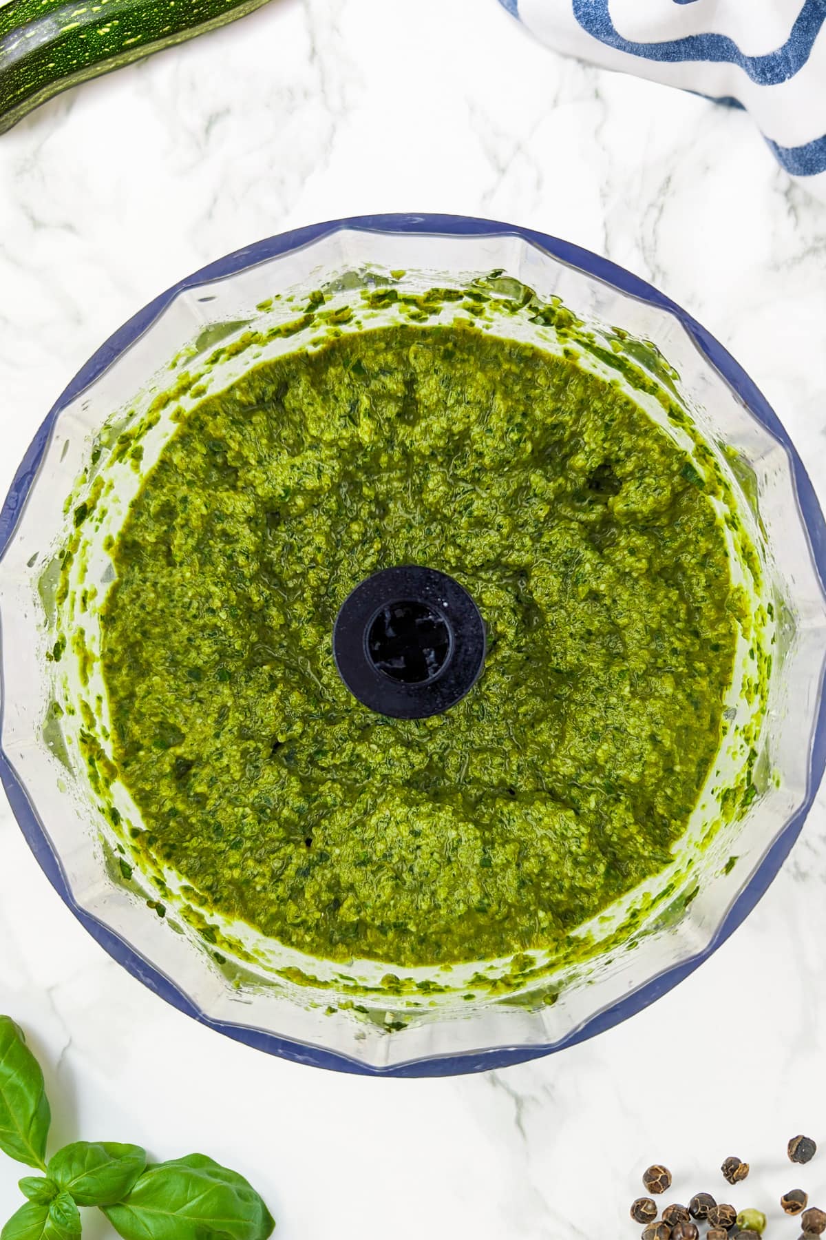 Top view of basil and zuchhini pesto on a mixing bowl on a white marble table.