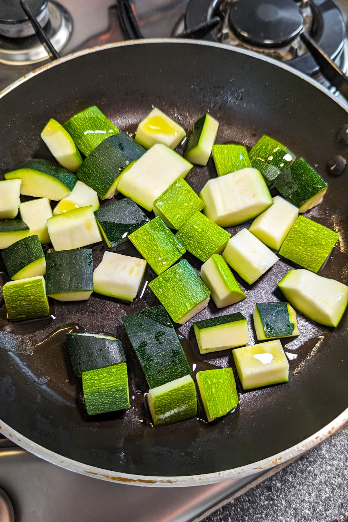 Frying zucchini pieces in a frying pan on the stove.