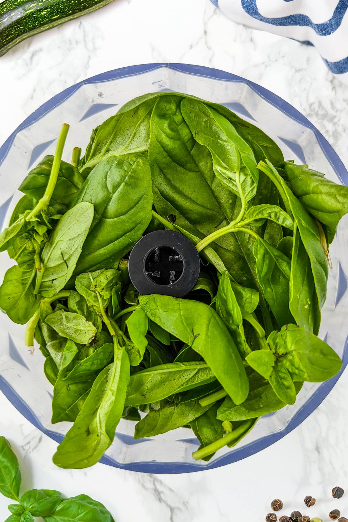 Fresh basil leaves in a table blender on a white marble table.
