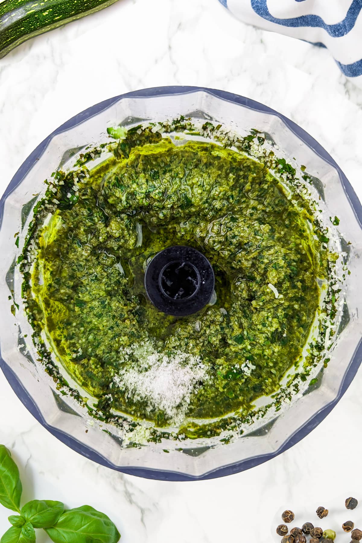 Top view of basil and zuchhini pesto on a mixing bowl on a white marble table.