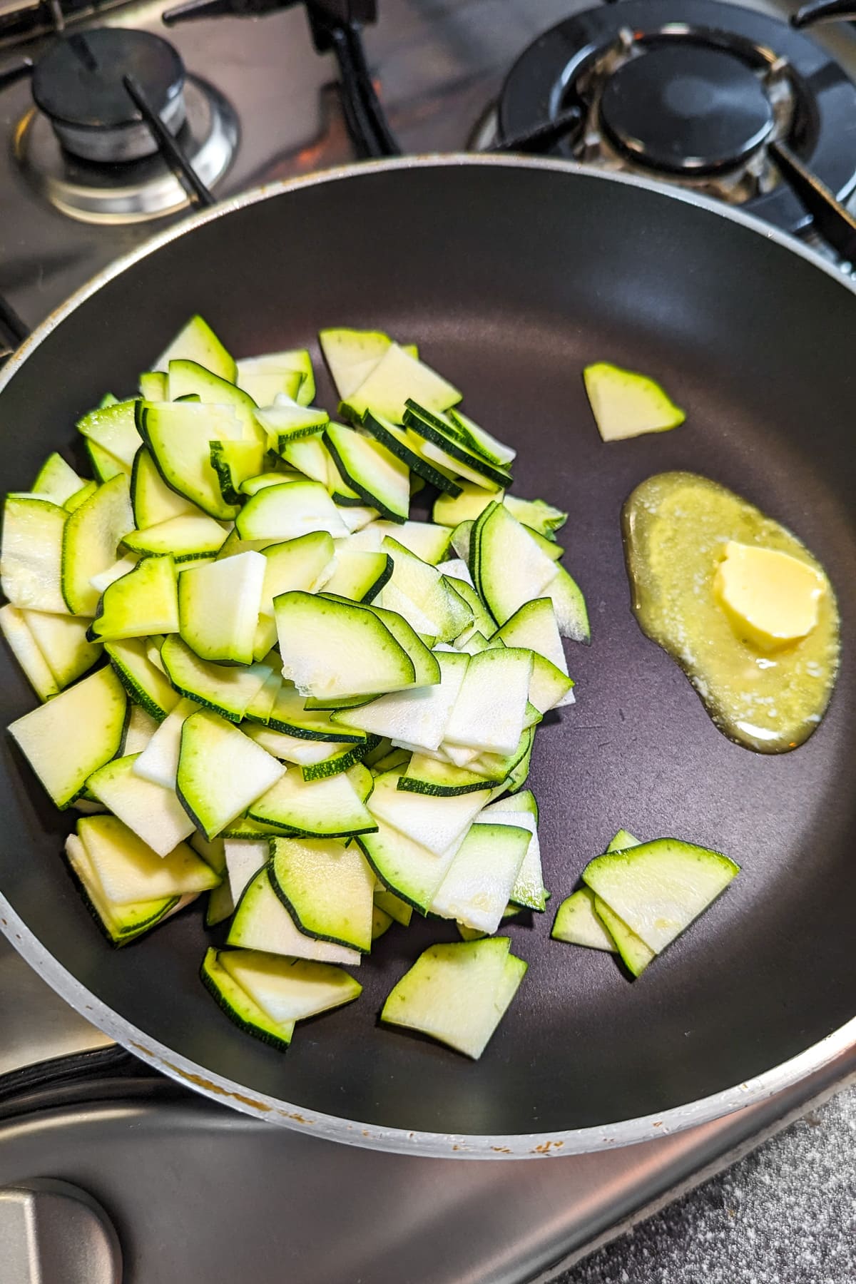 Frying pan with butter and zucchini slices in it.