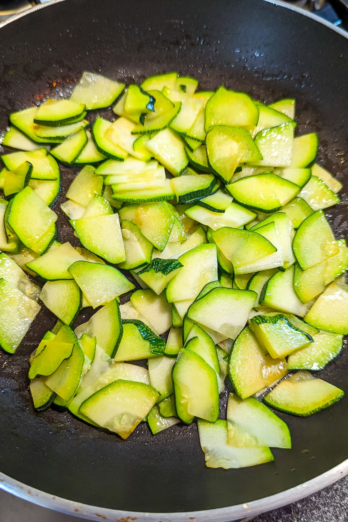 Frying zucchini slices in a frying pan on the stove.