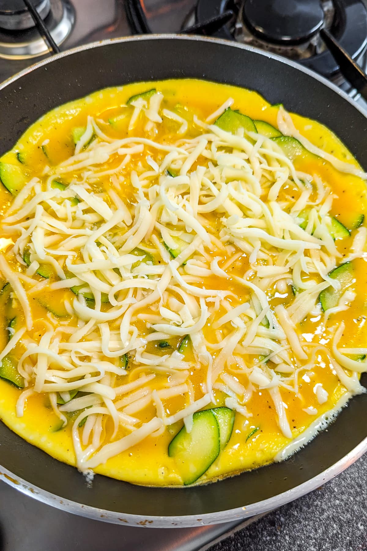Raw zucchini frittata in a frying pan on the stove.