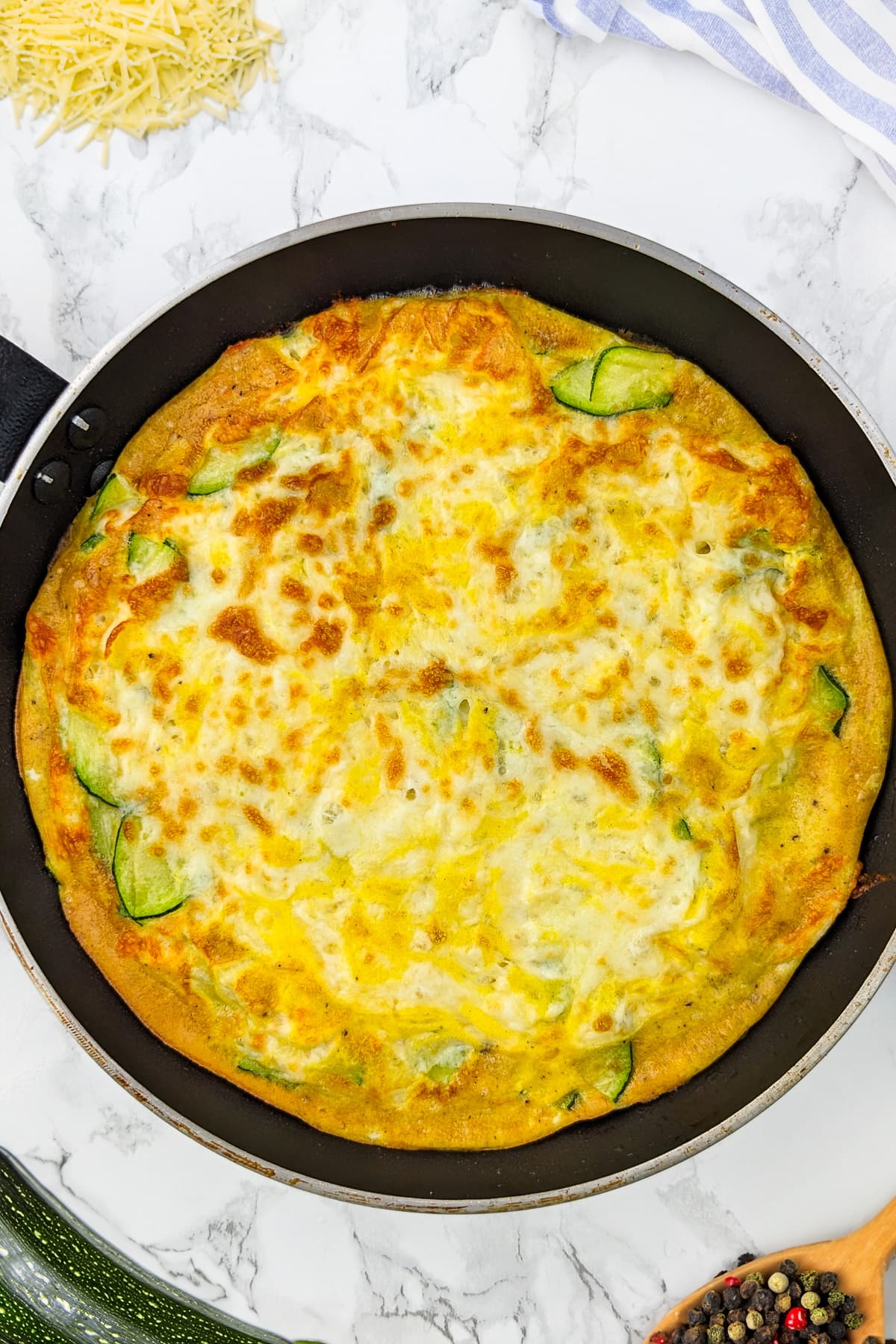 Top view of zucchini frittata with zucchini and basil leaves in a frying pan.