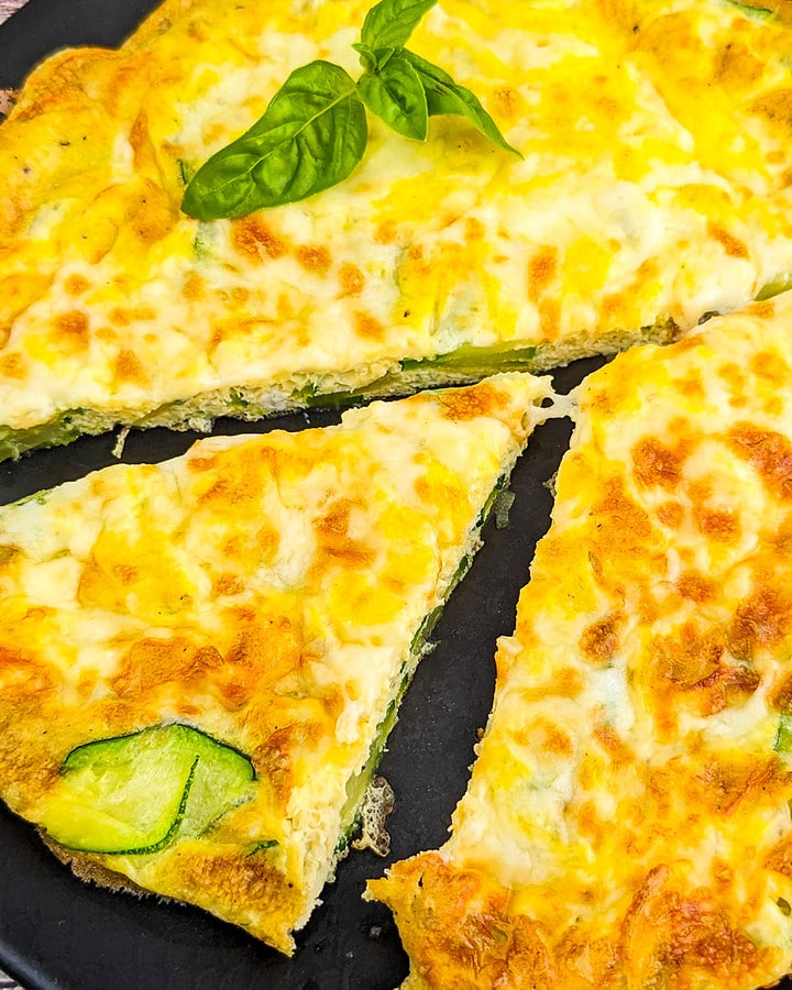 Close look of zucchini frittata with zucchini and basil leaves on a black plate.