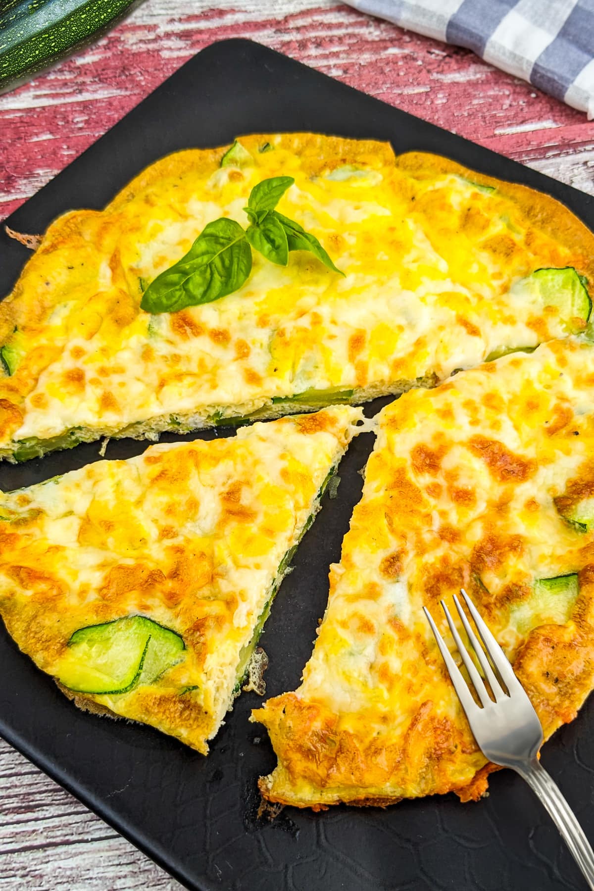 Top view of zucchini frittata with basil leaves served on a black plate.