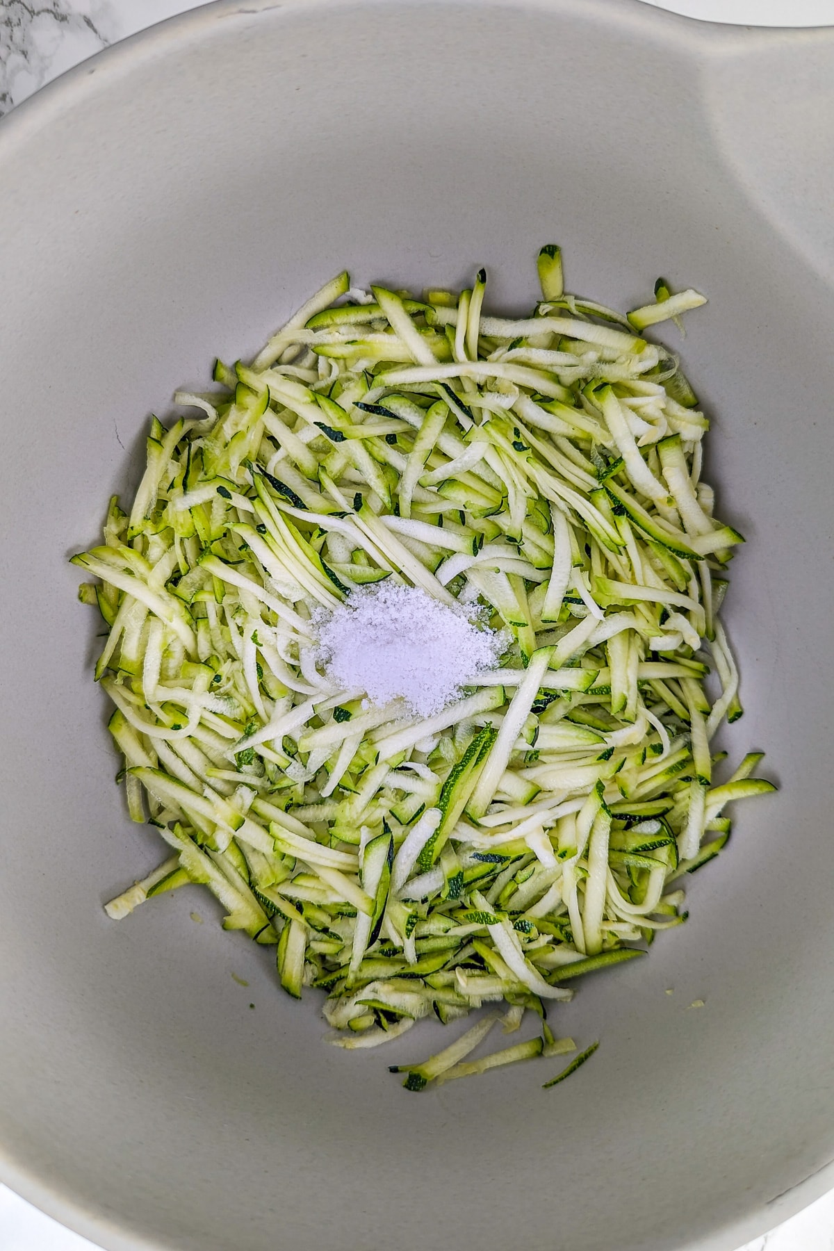 Grated zucchini with a pinch of salt in a deep bowl.