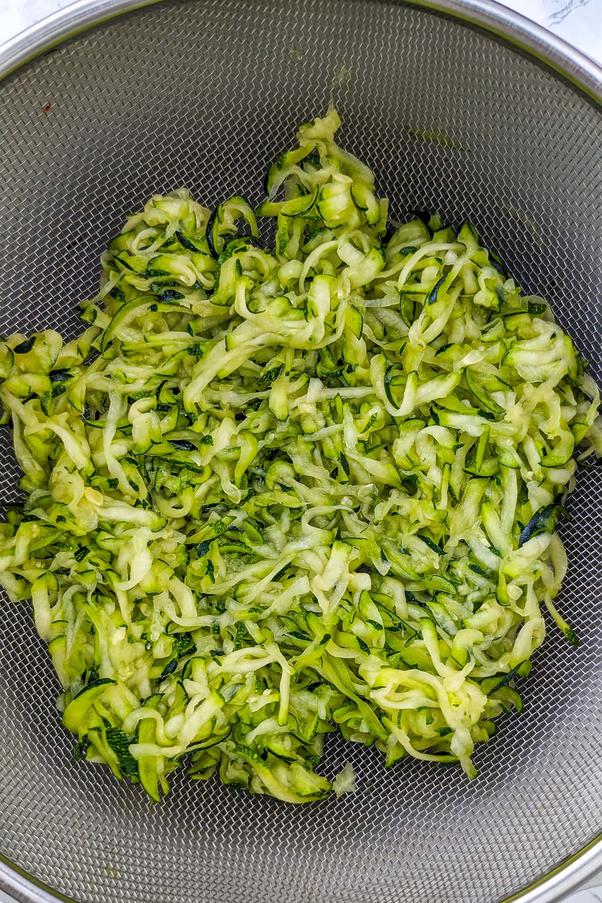 Top view of grated zucchini strained through a sieve.