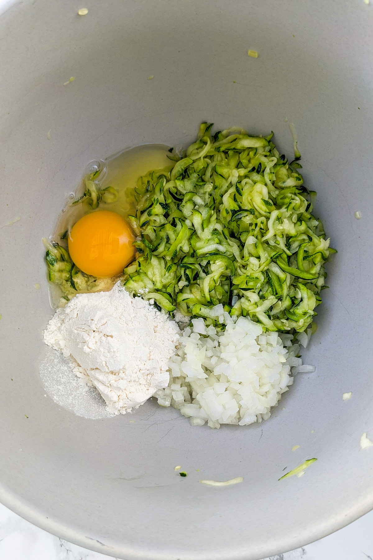 Shredded zuccchini, flour, onions, and an egg in a deep bowl.