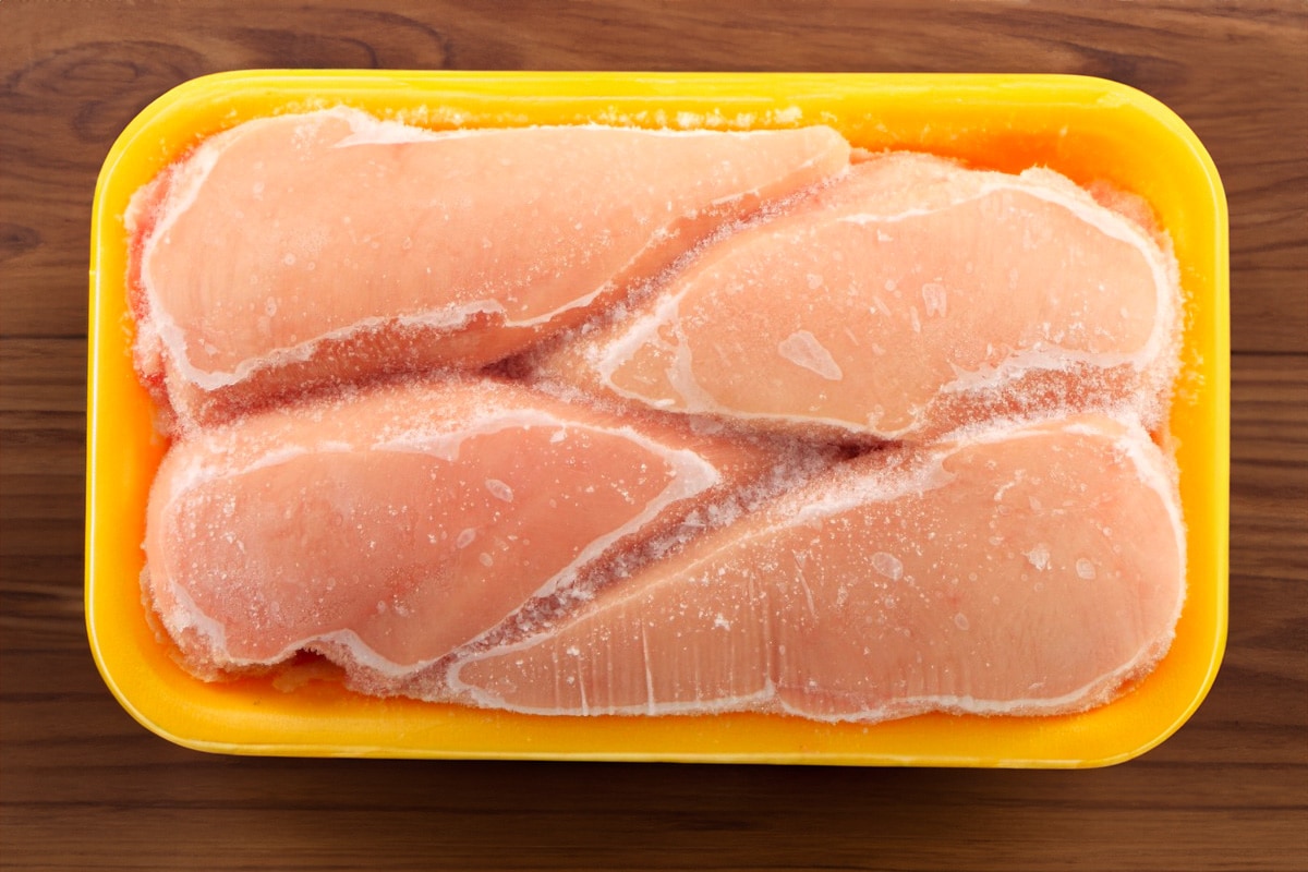 Top view of frozen chicken breast in a yellow plastic caserole.